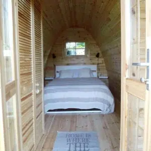 Wooden camping pod, view through entrance to a made-up bed