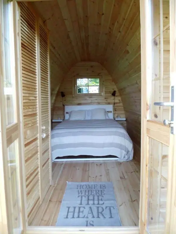 Wooden camping pod, view through entrance to a made-up bed