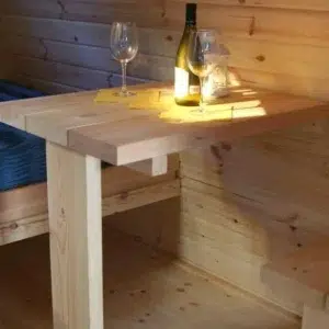 Wooden camping pod, wooden table beside a bed