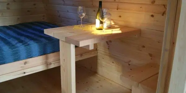 Wooden camping pod, wooden table beside a bed