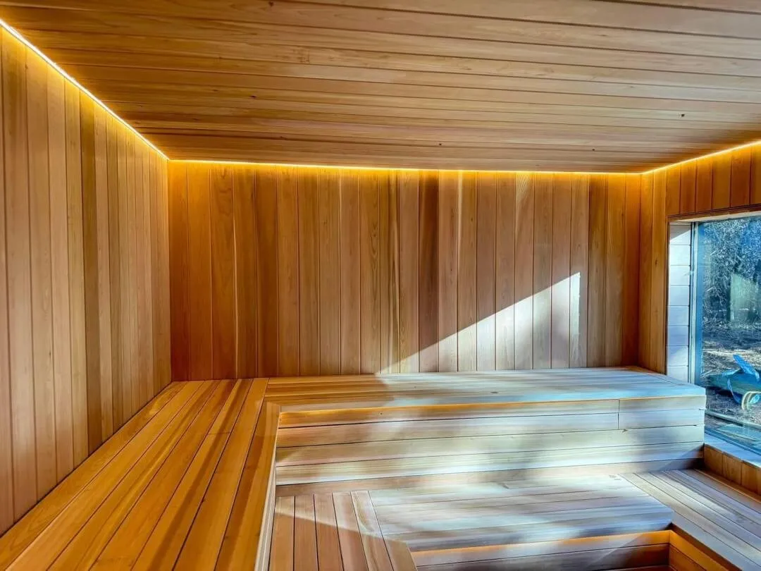 Finished sauna with tiered wooden benches, timber wall lining and a window