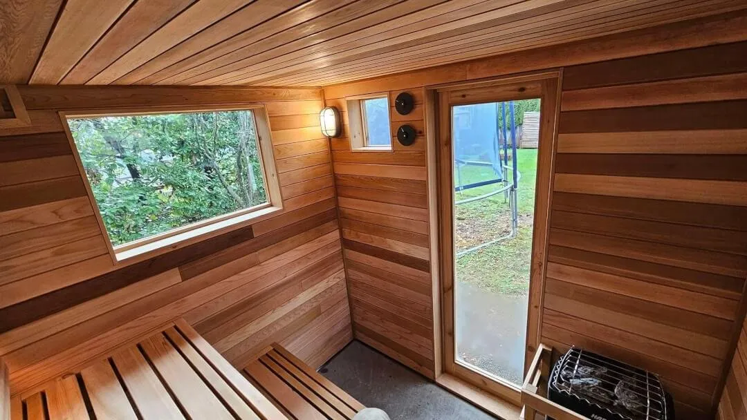 Wood-lined sauna with a large window, glass door and electric heater